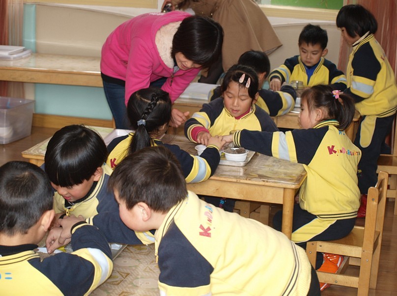 图为授课老师引导幼儿园学生自己动手尝试